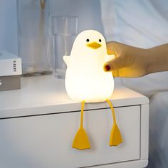 a person holding a light up to a penguin shaped object on a dresser top with other items in the background