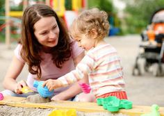 a woman and child playing with sand on a wooden table in front of a playground