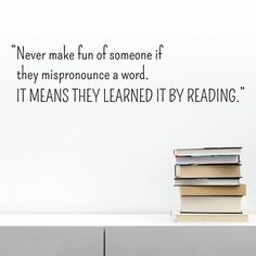 a stack of books sitting on top of a white table next to a wall with a quote