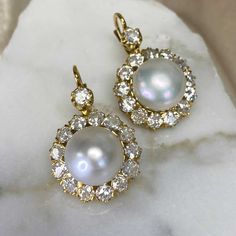 An amazing pear of cluster earrings featuring two saltwater natural round button pearls weighing 7.89 carats and 8.07 carats. Surrounding the pearls is a cluster of old European cut diamonds. The total approximate weight of the diamonds is 4.80 carats. These earrings are made in 18k yellow gold and have Euro-backs.
The measurements of the pearls are 11.20mm. The measurements including the diamond cluster are 18.40mm.
Ready to make them yours? Reserve them now or request more info! Wedding Round Pearl Earrings, Wedding Pearl Earrings Round Shape, Wedding Pearl Earrings With 17 Jewels, Luxury Yellow Gold Diamond Earrings With Pearl Drop, Classic Diamond Cluster Earrings, Pear-shaped, Yellow Gold Round Cut Diamond Cluster Earrings, Pearl Earrings With Diamond Accents, Round Cut, Luxury Yellow Gold Victorian Pearl Earrings, Luxury Vintage Yellow Gold Pearl Earrings