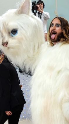 a man with long hair and blue eyes standing next to a white cat in a costume