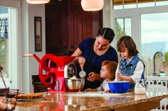 a woman and two children are making food in the kitchen with an electric blender