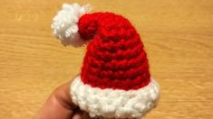 a small crocheted santa hat is held in someone's hand on a wooden surface