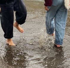 three people standing in the water with their feet up and one person holding an umbrella