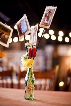 a vase filled with flowers sitting on top of a table next to pictures hanging from the ceiling