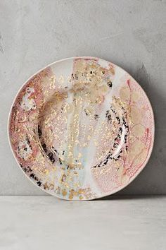 a white plate with gold splattered paint on it sitting against a gray wall