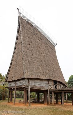 an old building with a thatched roof in the middle of a grassy area next to trees