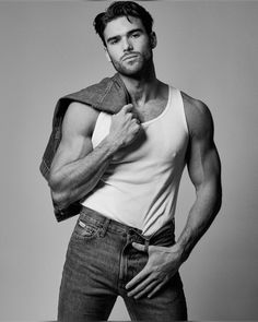 a man in jeans and a tank top is posing with his jacket over his shoulder