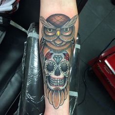 an owl with a diamond on its head is sitting next to a tattoo artist's arm