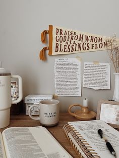 an open book sitting on top of a wooden table next to a cup and coffee mug