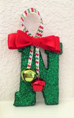 a green and red letter shaped ornament with a bell hanging from it's side