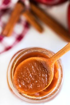 an apple cider is in a small glass jar with a wooden spoon full of caramel sauce