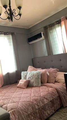 a bed with pink comforter and pillows in front of a ceiling mounted air conditioner