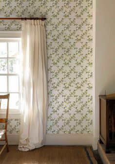 a chair sitting in front of a window next to a wall papered with flowers