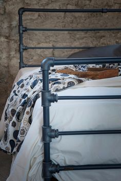 an iron bed frame with white pillows and blankets on it, in front of a stone wall