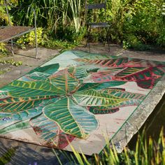 a colorful rug is on the ground in front of some trees and bushes with benches behind it