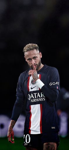 a man with tattoos on his face standing in front of a soccer field and making a hand gesture