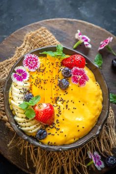 a bowl filled with fruit and cheese on top of a wooden table next to flowers