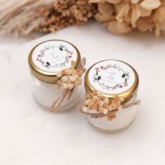 two white jars with gold lids are sitting on a table next to some dried flowers