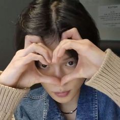 a woman making a heart with her hands while wearing a denim jacket and jeans shirt