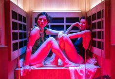 two women are sitting in a sauna with red light on the walls and floor