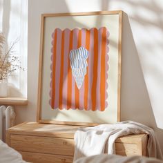 an orange and white art piece in a wooden frame on a dresser next to a window