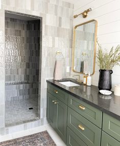 a bathroom with green cabinetry and marble counter tops, along with a gold framed mirror on the wall