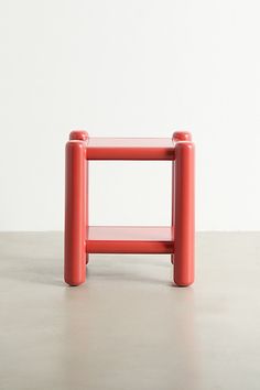 a small red stool sitting on top of a cement floor next to a white wall