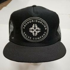 a black and white trucker hat with an embroidered logo on the front that says anchordarling valley company