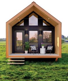 a small house with two chairs on the front porch and one sitting in the grass