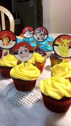 some cupcakes with yellow frosting and pokemon characters on them sitting on a table