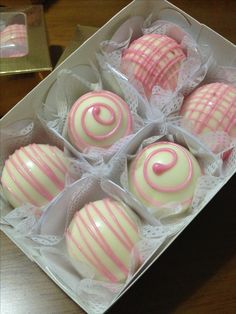 six pink and white decorated chocolates in a box on a table with other pastries