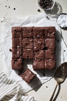 chocolate brownies cut into squares on top of parchment paper next to spoons and sugar