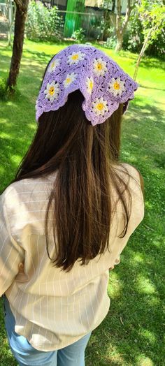 a woman standing in the grass wearing a purple crochet hat with daisies on it