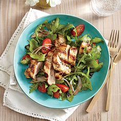 a blue plate topped with chicken, lettuce and tomato salad next to silverware