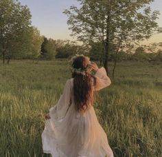 a woman in a white dress walking through tall grass with her back to the camera