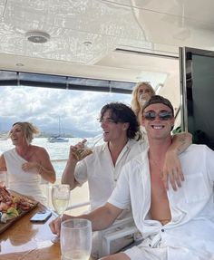 three people sitting at a table with drinks and food in front of them on a boat