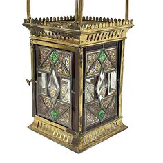 an ornately designed metal lantern with stained glass panels on the front and sides, set against a white background