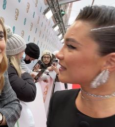 two women standing next to each other on a red carpet with people in the background