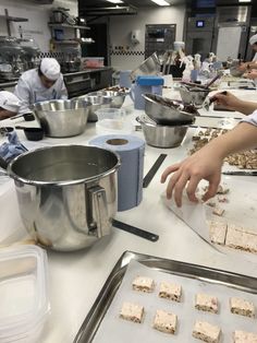 several people in a kitchen preparing food on trays and pans with utensils