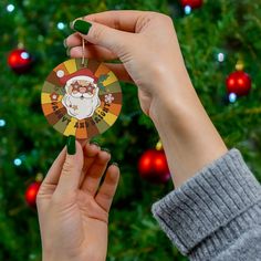 a person holding up a christmas ornament in front of a christmas tree