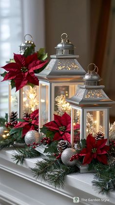 three lit up lanterns with poinsettias and pine cones on the mantel