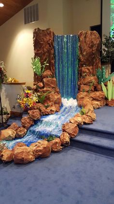 an indoor waterfall is shown in the center of a room with blue carpet and steps leading up to it