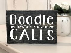 a wooden sign that says doodie calls on it next to a vase with flowers