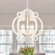 a white chandelier hanging from the ceiling in a room with windows and potted plants