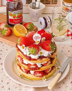 a stack of pancakes with strawberries and whipped cream on top sitting on a table