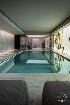 an indoor swimming pool with no people in the water and two lounge chairs next to it