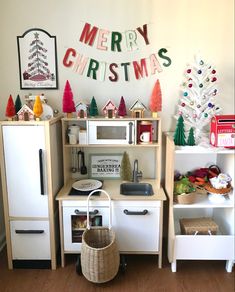 there is a toy kitchen set with christmas decorations on the wall behind it and a basket in front of it