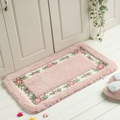 a pink rug with flowers on it next to two slippers and a teddy bear