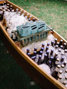 a wooden boat filled with lots of bottles and ice cubes on top of grass